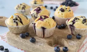 Frisch gebackene Blaubeermuffins, die nach den besten Muffin Rezepten aussehen, liegen auf einem Holzbrett.