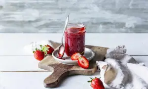 Frische Erdbeeren und selbstgemachte Erdbeermarmelade aus dem Thermomix auf einem Holzbrett.