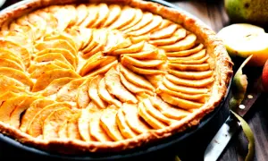 Ein wunderschönes Apfeltarte Rezept, das mit dünn geschnittenen Äpfeln belegt ist. Daneben liegen frische Äpfel und ein Messer.