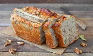 Saftiger bananenkuchen vegan, mit Nüssen und Bananenstücken, auf einem Holztisch.
