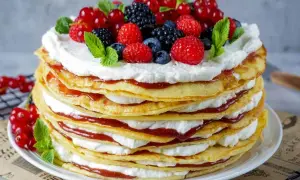 Eine hohe Pfannkuchen Torte mit Sahne und roter Marmelade, gekrönt mit frischen Beeren und Minze.