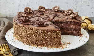 Schokoladentorte mit Ferrero Rocher verziert, die Seiten sind mit gehackten Nüssen bedeckt. Ein Stück fehlt, was Lust auf mehr macht.