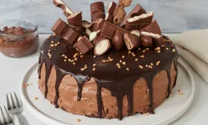 Eine üppige Nutella Torte, dekoriert mit Schokoriegeln und Nüssen. Daneben ein Glas Nutella.