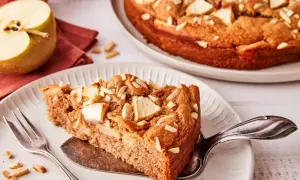 Ein Stück saftiger apfelkuchen ohne zucker, garniert mit Mandelblättchen. Daneben ein halber Apfel und eine Gabel.