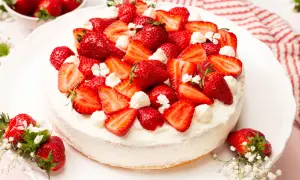 Eine köstliche Erdbeer-Sahne-Torte, üppig belegt mit frischen Erdbeerscheiben und Sahnetupfern, verziert mit kleinen weißen Blüten.