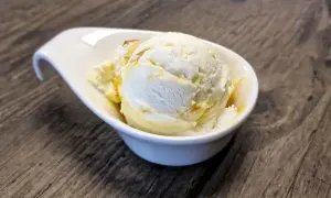 Ein cremiges Eis, das nach Buttermilch schmeckt, in einer weißen Schale auf Holztisch.
