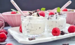 Zwei Gläser mit cremigem Dessert, garniert mit Himbeeren und Schokostückchen. Ein leckeres Herrencreme Rezept zum Nachmachen.