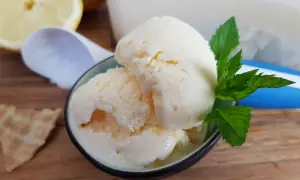 Erfrischendes zitroneneis mit joghurt, garniert mit Minze, daneben eine Waffel und Zitronenspalten.