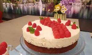 Himbeer-Mascarpone-Torte mit frischen Beeren und Minze, dekoriert mit einem Blumenstrauß im Hintergrund.