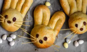 Osterhasen backen mit Hefeteig: Süße Hasen aus Teig mit Rosinenaugen und Spaghetti-Schnurrhaaren, umgeben von bunten Ostereiern.
