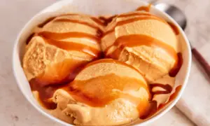 Drei Kugeln cremiges Karamell-Eis, übergossen mit flüssigem Karamell, in einer weißen Schüssel.