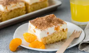 Ein Stück saftiger Fanta Kuchen mit cremiger Füllung, Mandarinenstücken und Zimt bestreut, daneben ein Glas Fanta.