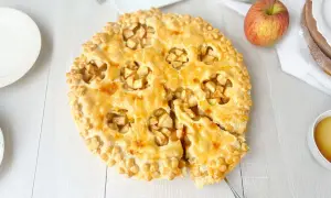 Goldbrauner Apfelkuchen mit Blätterteig-Dekor, ein Stück herausgeschnitten.
