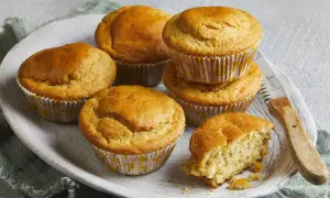 Goldbraune Buttermilch Muffins auf einem Holzteller, einer davon angebrochen, mit einem Messer daneben.