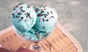 Zwei Kugeln blaues Eis mit bunten Streuseln in einem Glas auf einem Holzuntersetzer.