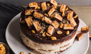 Eine köstliche Snickers Torte mit Schokoladenglasur, Erdnüssen und vielen Snickers-Stücken obendrauf.