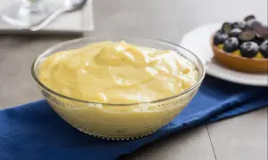 Cremige Crema Pasticcera in einer Glasschüssel, verfeinert mit Vanille. Daneben ein Törtchen mit Blaubeeren.