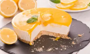 Ein Anschnitt eines cremigen Lemon Cheesecake mit Zitronenscheiben und Minze garniert.