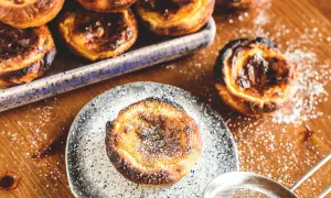 Köstliche, karamellisierte Pastéis de Nata, bestäubt mit Puderzucker, warten auf dem Holztisch.