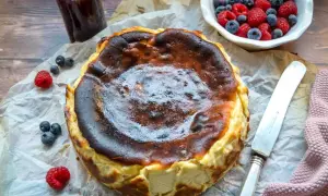 Ein perfekt gebackener San Sebastian Cheesecake mit karamellisierter Kruste, garniert mit frischen Beeren und einem Glas Marmelade.