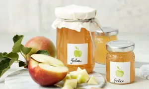 Zwei Gläser mit selbstgemachtem Apfelgelee, daneben frische Äpfel und Apfelstücke. Ein leckeres Apfelgelee Rezept zum Nachmachen.