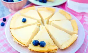 Ein cremiger, kalorienarmer Kuchen mit Blaubeeren, der auf einem rosa karierten Tuch serviert wird.