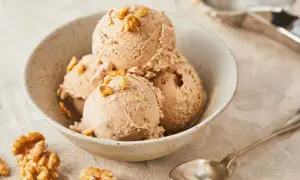 Schüssel mit Walnusseis, garniert mit Walnussstückchen. Ein Löffel und Walnüsse liegen daneben. Perfekt für ein Walnusseis Rezept.