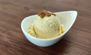 Cremiges Eis mit Eigelb, garniert mit karamellisierten Stückchen, in einer weißen Schale auf Holzhintergrund.