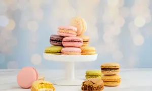 Bunte Macarons auf einem weißen Tortenständer, einige angeschnitten, vor unscharfem Bokeh-Hintergrund.