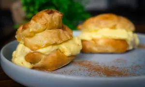Zwei Windbeutel-Desserts mit cremiger Füllung, bestäubt mit Zimt auf einem Teller.