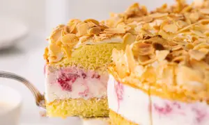 Ein Stück himmelstorte mit himbeeren wird mit einer Gabel herausgehoben. Die Torte ist mit Mandelsplittern bestreut.