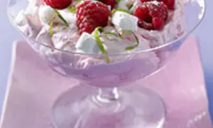 Himbeer-Mascarpone-Creme in einem Glas, garniert mit frischen Himbeeren, kleinen weißen Baiserstückchen und Zitronenmelisse.