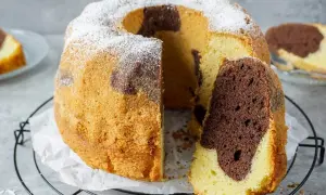 Ein saftiger Marmorkuchen, der zeigt, wie einfach backen sein kann. Mit Puderzucker bestäubt und einem Stück herausgeschnitten.
