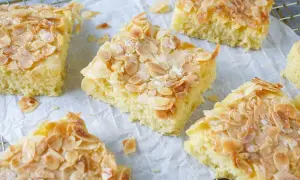 Saftiger Buttermilch Kuchen mit knusprigen Mandelblättchen und Zucker bestreut, auf Backpapier und einem Gitterrost.