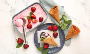 Erdbeer-Fruchteis selber machen: Ein Löffel Eis in einem Waffelhörnchen, garniert mit frischen Erdbeeren und Minze. Daneben eine Schale mit Eis und Erdbeeren.