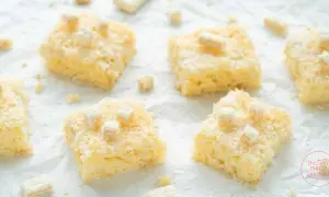 Saftige Stücke Buttermilch Kokos Kuchen, bestreut mit Kokosraspeln und kleinen weißen Würfeln, verlocken zum Genuss.