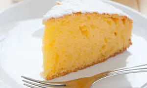 Ein saftiges Stück Vanille Kuchen, bestäubt mit Puderzucker, wartet auf dem Teller neben einer Gabel.