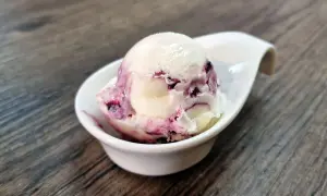 Cremiges Cheesecake Eis mit fruchtigen Beerenwirbeln in einer weißen Schale auf Holztisch.