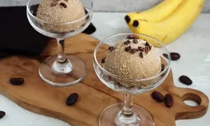 Zwei Gläser mit cremigem Apfel Zimt Eis, garniert mit Kakaonibs. Bananen im Hintergrund.