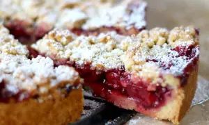 Saftiger kirschkuchen mit streusel, bestäubt mit Puderzucker. Ein Stück wurde herausgeschnitten, um die roten Kirschen zu enthüllen.