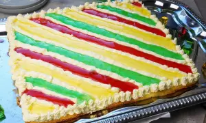 Bunte Philadelphia Torte mit Waldmeister-Aroma, dekoriert mit Sahnetuffs und roten Fruchtstreifen.