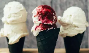 Drei Eiswaffeln, zwei mit cremigem veganem Vanilleeis, eine mit Beerensoße.