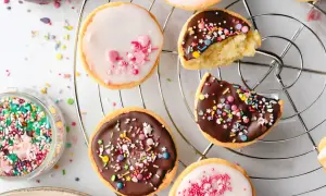 Bunte mini Amerikaner mit Schokoladen- und Zuckerguss, bestreut mit Streuseln und Herzen, auf einem Kuchengitter.