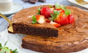 Ein saftiger brownie kuchen, garniert mit frischen Erdbeeren und Minze. Ein Stück wird mit einem goldenen Tortenheber herausgehoben.