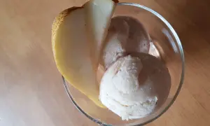 Ein Glas mit cremigem birnen eis, garniert mit einer frischen Birnenspalte, steht auf einem Holztisch.