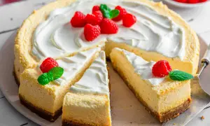 Ein New York Cheesecake, dekoriert mit frischen Himbeeren und Minze, wartet darauf, genossen zu werden.