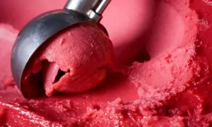 Ein Löffel nimmt eine Kugel leuchtend rotes Eis auf. Es sieht aus wie ein köstliches Eis mit Ei, das auf der Zunge zergeht.