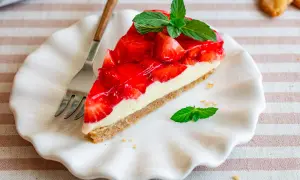 Ein Stück Erdbeer-no-bake-cheesecake mit frischer Minze auf einem weißen Teller, daneben eine Gabel.