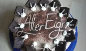 Eine After Eight Torte mit Schokoladenquadraten und Sahnetuffs. Der Schriftzug "After Eight" ist in Kakao auf die Torte gestreut.