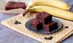Saftige Bananen-Brownies auf einem gelben Tuch, daneben reife Bananen. Ein Genuss!